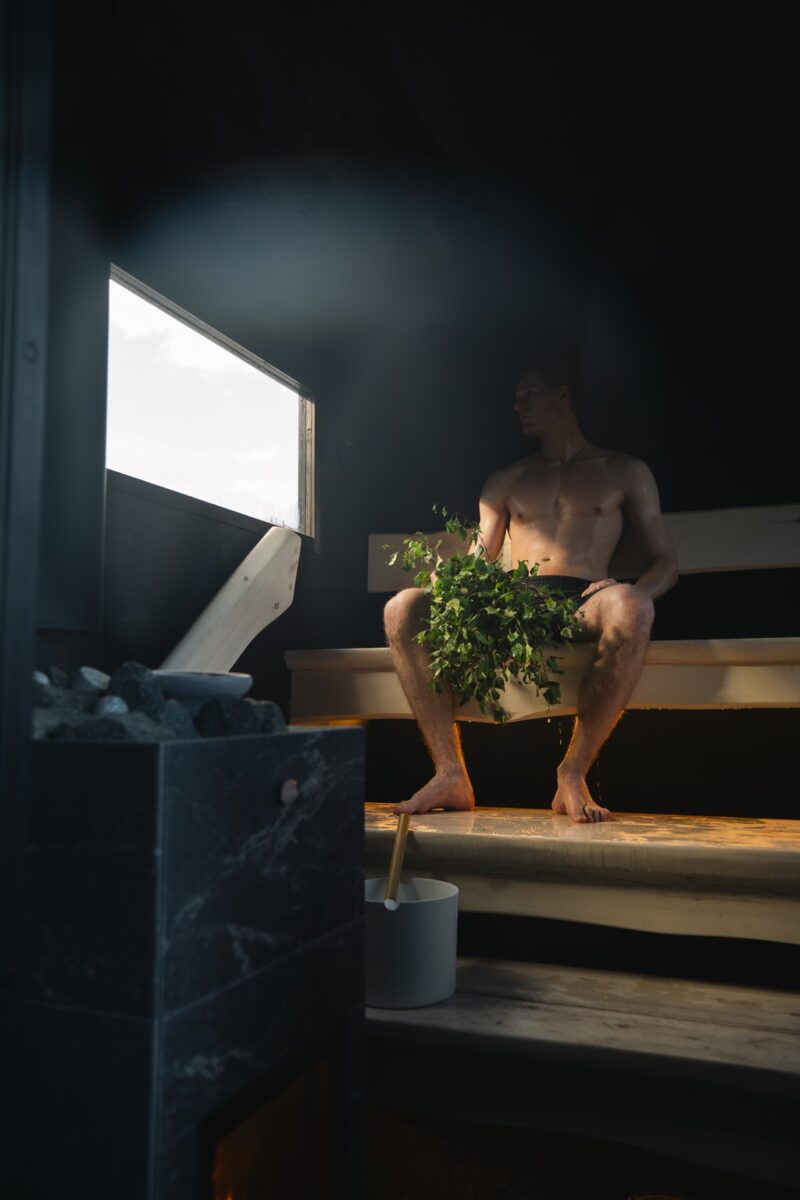Man in a finnish sauna holding a traditional sauna whisk